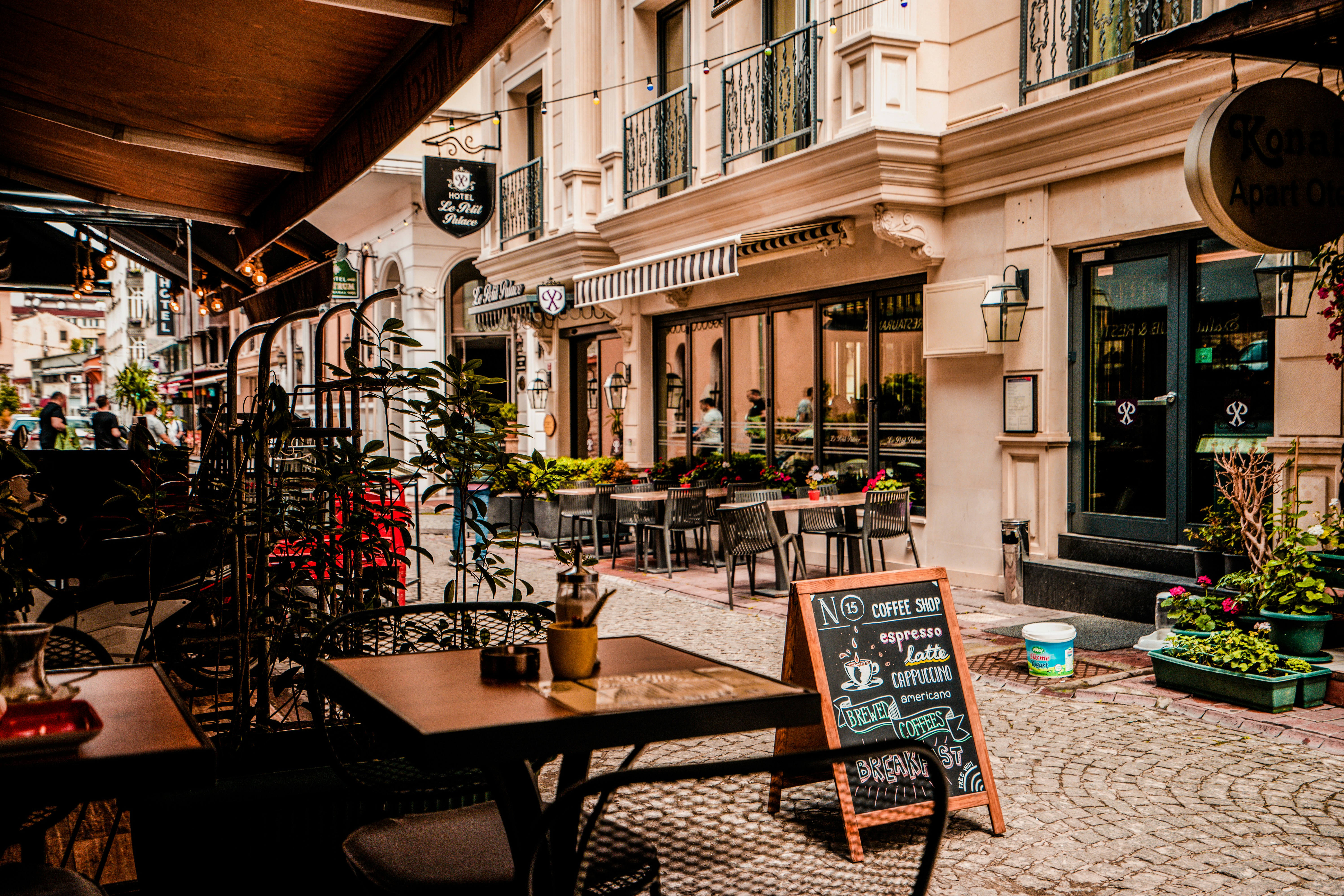 A café terrace in front of a hotel, with a chalkboard menu listing coffee and breakfast.